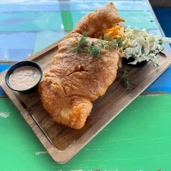 Crispy fried fish with fries, coleslaw, and dipping sauce on a wooden tray at Island Pig and Fish.