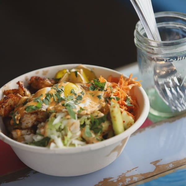 A close-up of a seafood bowl with shrimp, fried eggs, vegetables, and sauce, next to a mason jar.