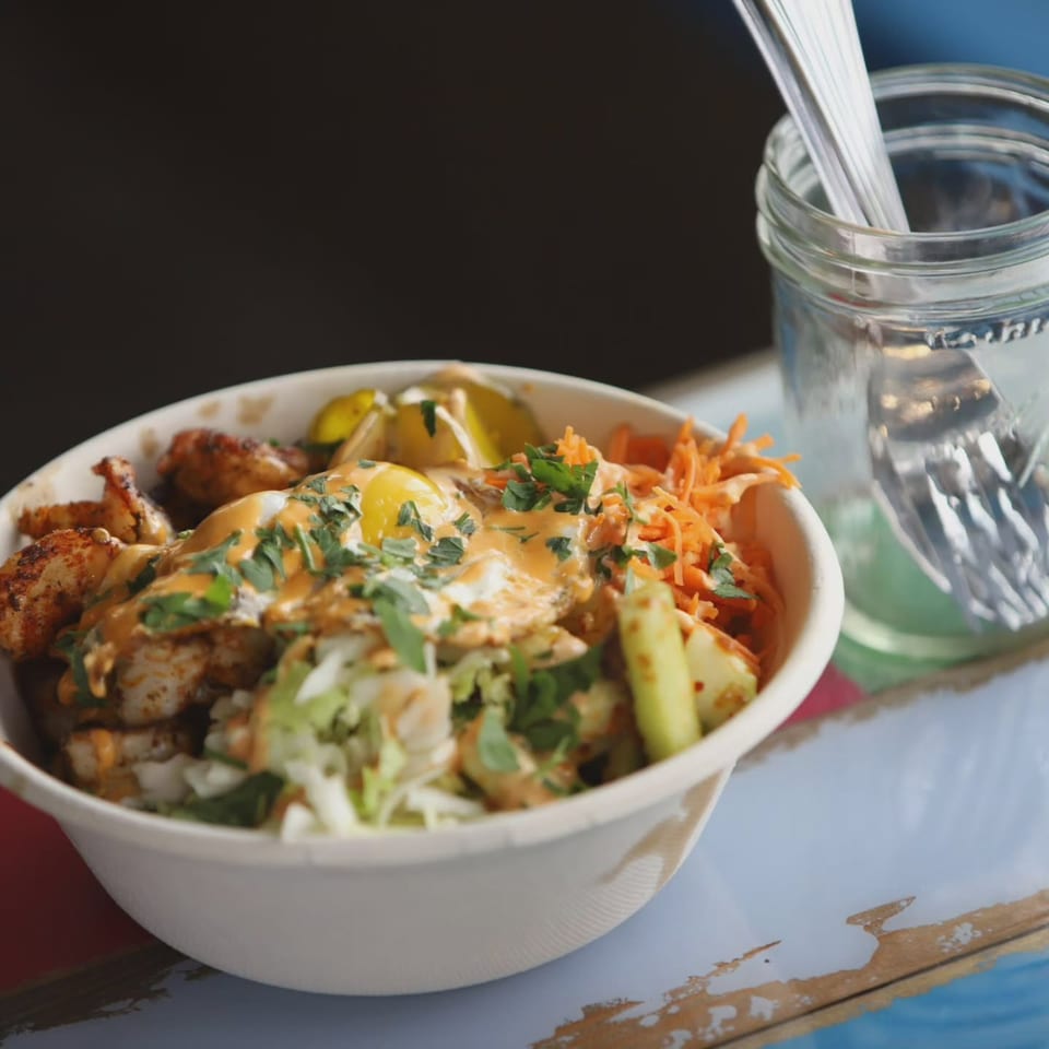 A close-up of a seafood bowl with shrimp, fried eggs, vegetables, and sauce, next to a mason jar.